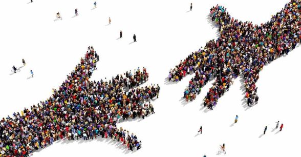 Two hands reaching out toward the other. The hands are made up of a large group of people standing in the shape of the hands.