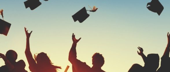 A group of people, all silhouettes, throw graduation caps in the air in a celebratory fashion. They are backlit by the glow of sunlight.