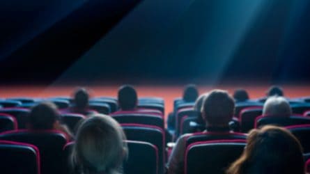People in a movie theater, sitting in seats. The photo is from behind so you can only see the backs of heads.