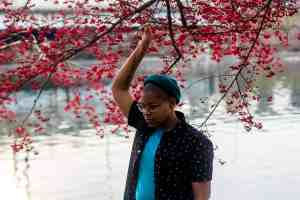 Photo of Cyree standing in front of water under a tree with red leaves.