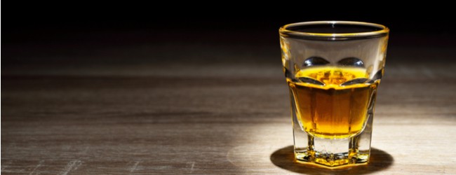 A single glass of whiskey sitting on a wood table.