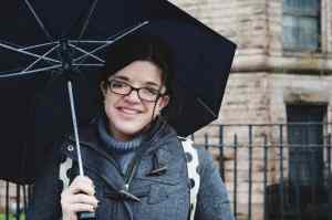 Photo of Ariel Henley in a gray jacket, smiling and holding a black umbrella.