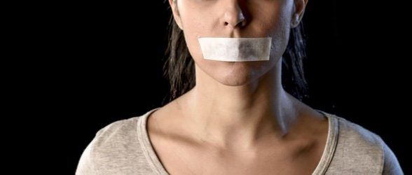 A female-presenting person shown from the nose to the neck, with duct tape over her mouth, indicating silence.