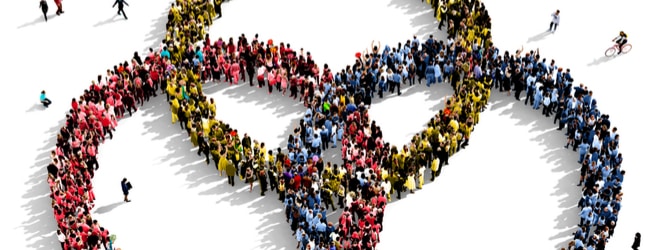 Three partially formed circle made up of an aerial view of people. In one circle, people are dressed in red, in another, they're dressed in blue, and in the third, green. Where the circle intersect, the clothing is multicolored.