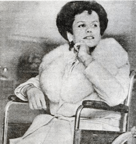 Bobbie Lea Bennett, a trans woman, sits in a wheelchair. She is wearing a white coat with a fur collar.