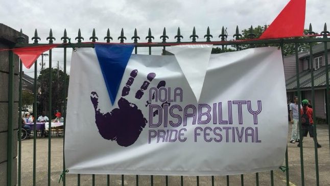 Sign with a handprint that reads "NOLA Disability Pride Festival" hanging on a wrought iron gate.