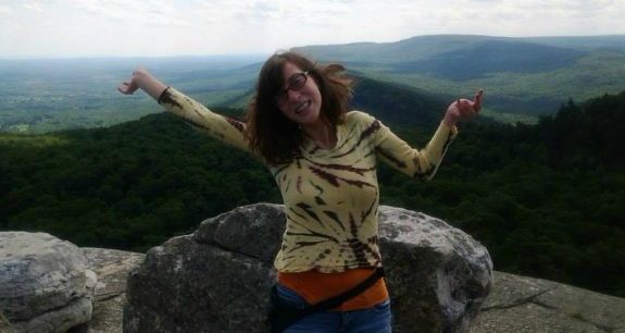 Hannah posing before a skyline and mountain, arms up in the air.