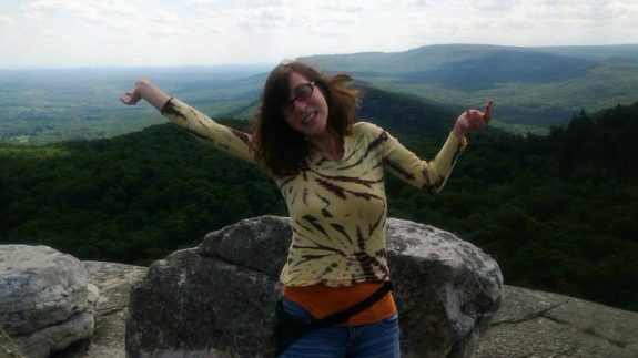 Hannah posing before a skyline and mountain, arms up in the air.