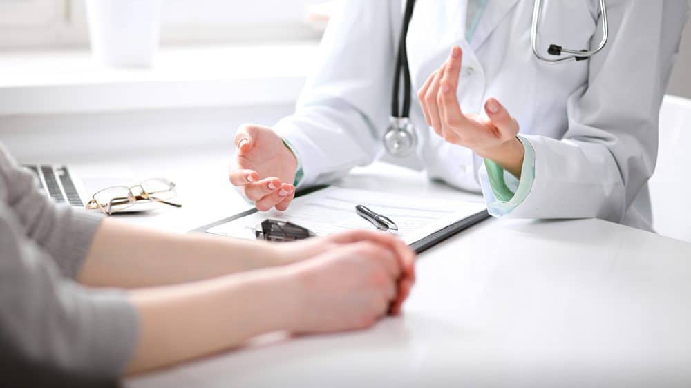 Close up of doctor and patient sitting at the desk near the window in hospital