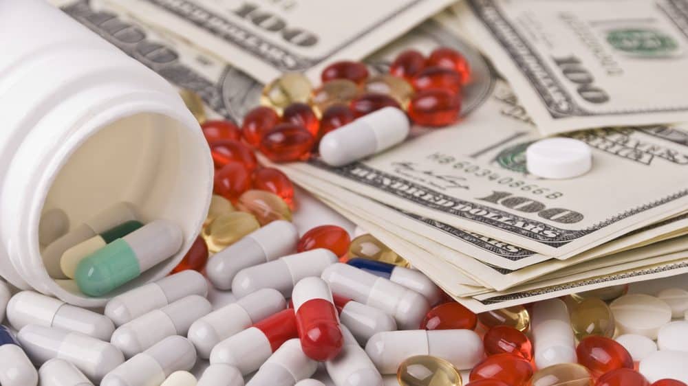 A spilled bottle of different types of medicine on top of $100 bills.