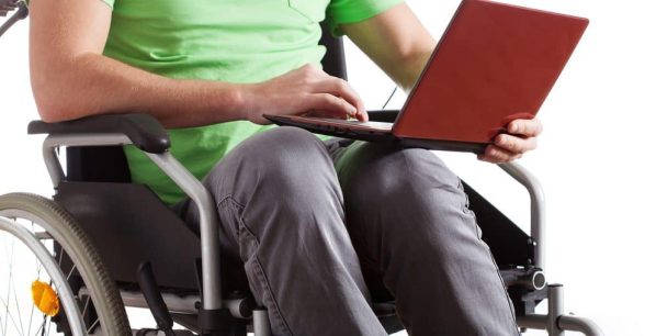 A person in a manual wheelchair holds a red laptop in their lap.