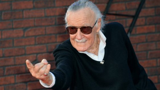 Photo of Stan Lee in a black suit and sunglasses, pointing his finger forward.