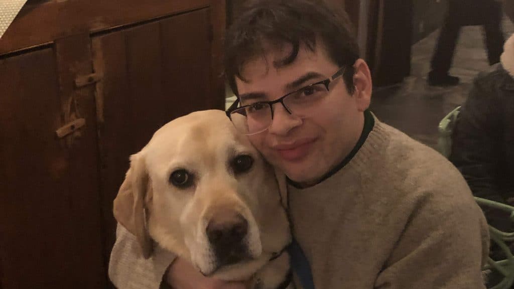 Photo of Ryan hugging his service dog, PIco.