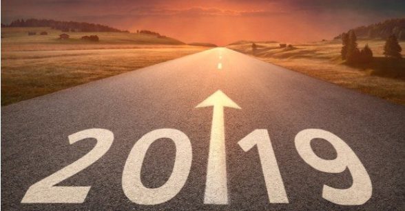 Idyllic open road leading toward setting sun with 2019 written on the road with a big forward pointing arrow.