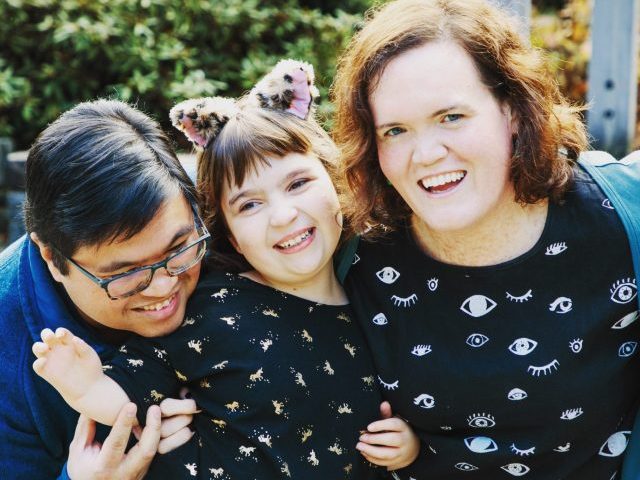 Carrie, her partner, and child are smiling and facing the camera.