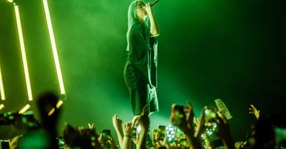 green toned photo of Billie Eilish singing on stage to a crowd