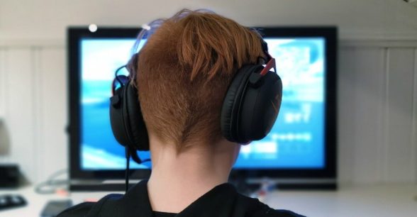 Photo of person wearing headphones and a sweatshirt, sitting in front of a computer screen