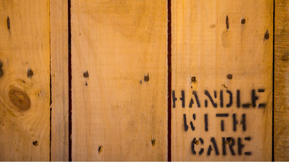 Wooden shipping crate with the words "handle with care" printed on it.