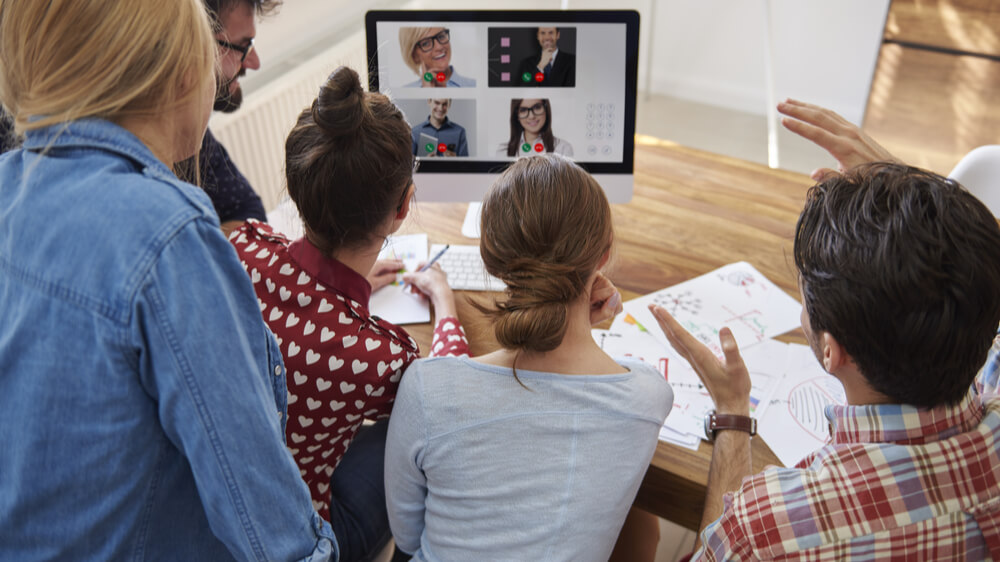Group of people around a computer at a desk, videoconferencing