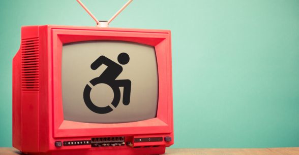 A retro red television with antennae sitting on a wooden surface in front of a mint green wall. The TV has an accessible icon on it.