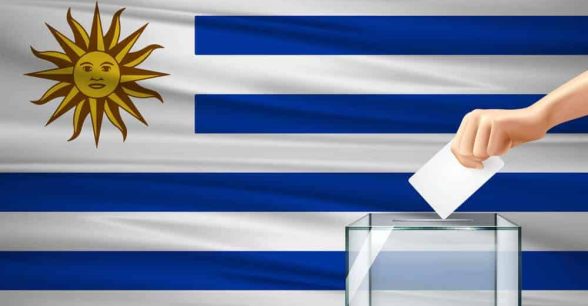 Uruguayan flag with a ballot box in front of it and a hand dropping in the ballot.