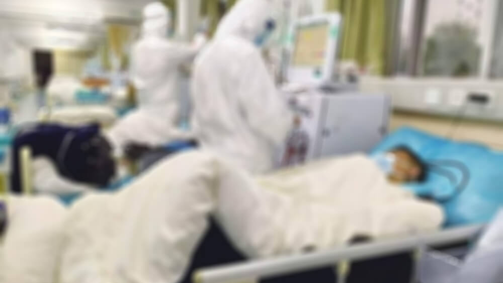 Blurred photo of medical professionals in protective gear treating a patient.