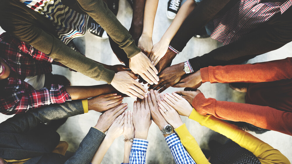 Photo of people of different skin colors standing in a circle, all holding their hands together