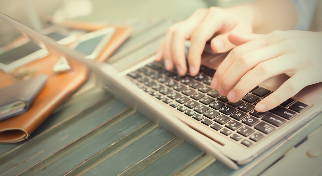 Hands typing on a laptop resting on a wooden surface.