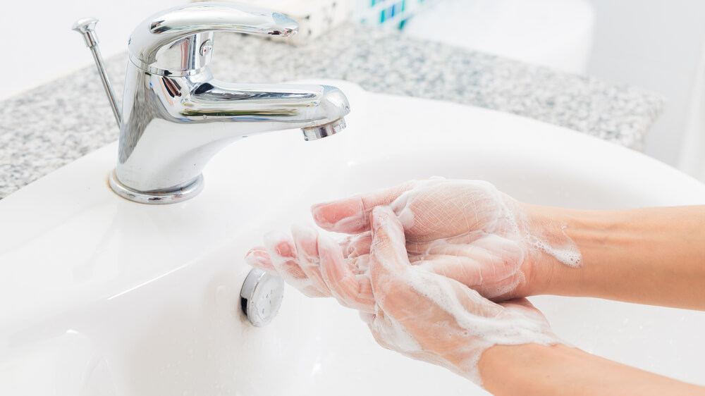 Photo of hands covered in soap under a sink with running water.