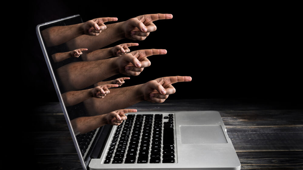 Hands with fingers pointing outward coming out of a laptop screen