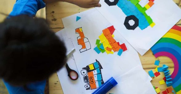 A photo taken from above of a kid doing crafts, making rainbows and drawing trucks.