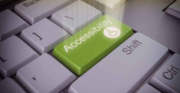 Computer keyboard with a big green key that says "accessibility" and has a small access symbol. There's a spotlight shining on the accessibility key.
