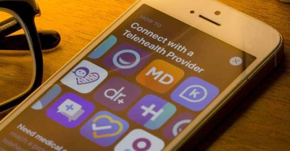 Mobile app icons of assorted telehealth providers from the App Store are seen on a smartphone.