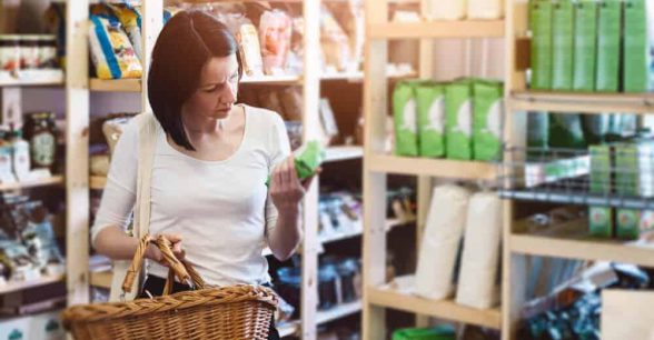 Woman in a grocery store holding a basket in one hand and a product in the other hand, reading its label.