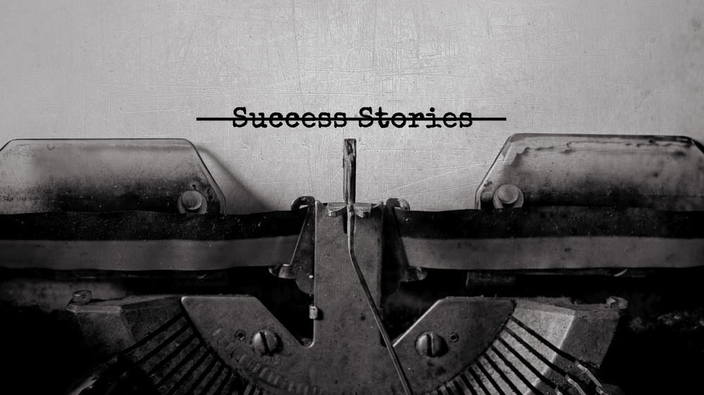 A close-up of a typewriter with a piece of paper in it that says "success stories." The words are crossed out with a black line.