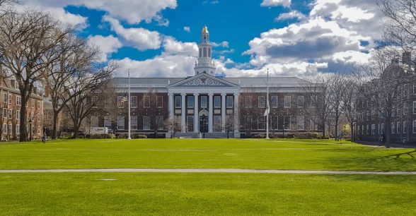 A photo of a building on the Harvard campus, surrounded by a bright blue cloudy sky and bright green grass.