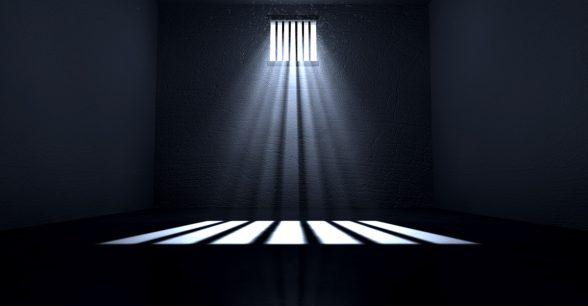 An old jail cell interior with barred up window with light rays penetrating through it reflecting the image on the floor