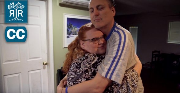 A middle aged white man hugs a white woman with red hair.