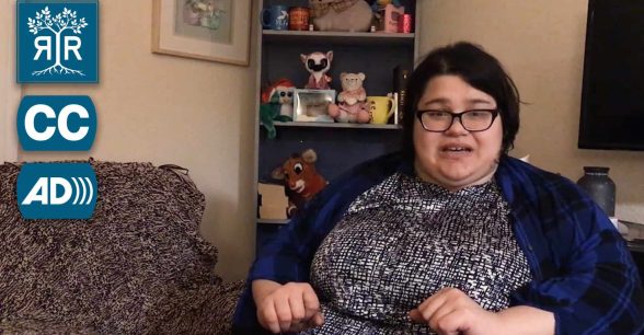 Yolanda is talking to the camera, she is sitting in front of a bookshelf with stuffed animals.