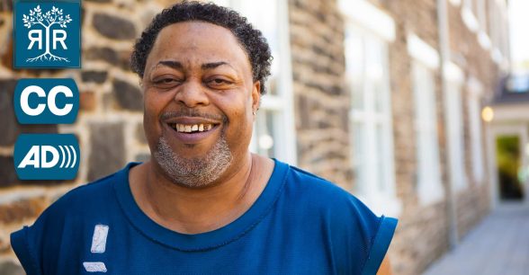 A middle aged man is standing next to a brick building, smiling at the camera.