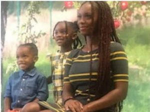 An African American woman sits on a chair next to two of her children.