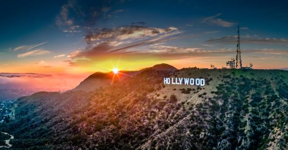 The famous Hollywood sign in big, white block letters set on a mountainous, grassy terrain during either a sunrise or sunset.