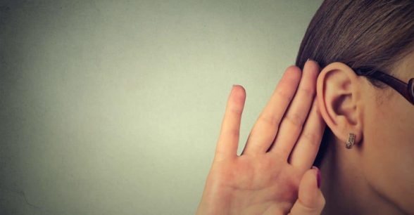 A fair-skinned person with brown hair, face partially not visible because it's off-camera, holds their hand up to their ear, as though listening to something.