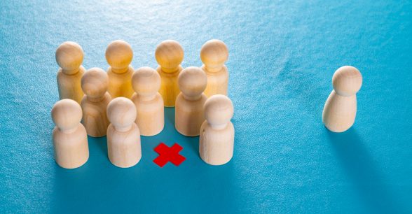 A group of 10 representative wooden figures cluster together on a blue background. A red x marks an empty space in the group. A single wooden figure sits to the right of the group, alone.