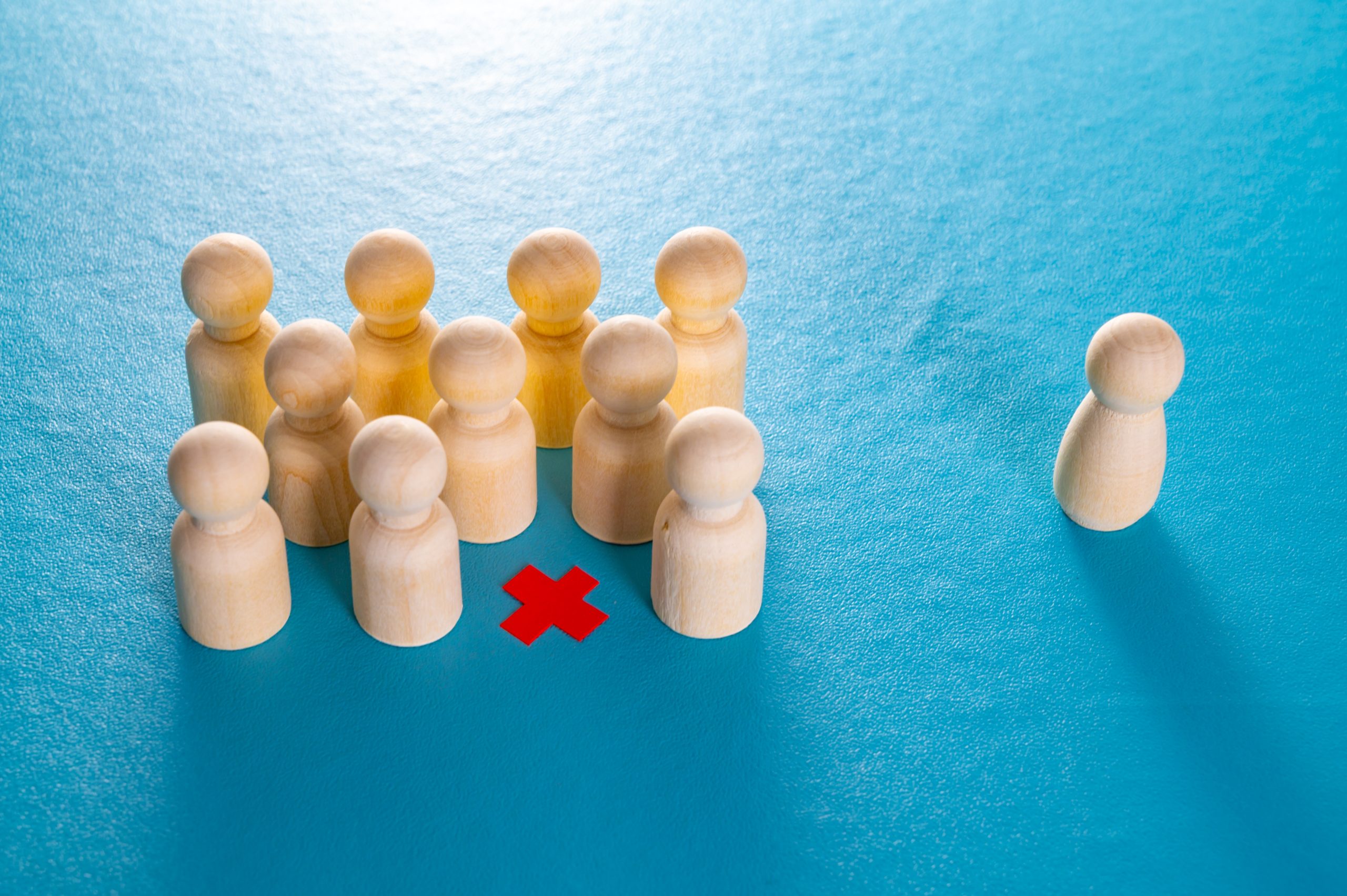A group of 10 representative wooden figures cluster together on a blue background. A red x marks an empty space in the group. A single wooden figure sits to the right of the group, alone.